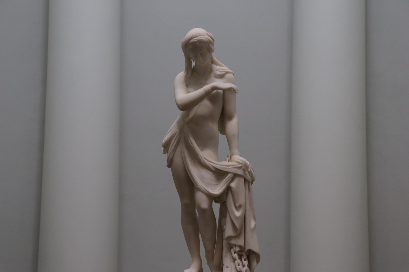 A small marble figure of a draped woman, standing between two pale columns