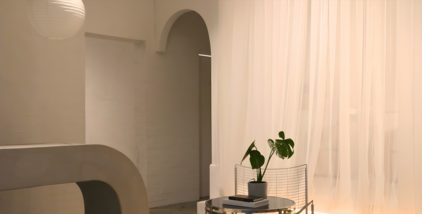The salon interior: plaster arches, a curved bench, sheer curtains and warm light