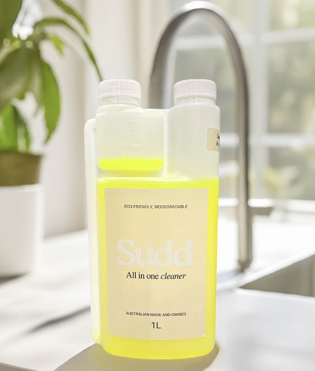 A one-litre bottle of SÜDD All in One Cleaner concentrate on a kitchen bench by the tap
