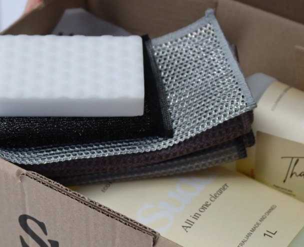 A SÜDD box opened to show cleaning cloths, a scrubbing sponge and a one-litre All in One Cleaner